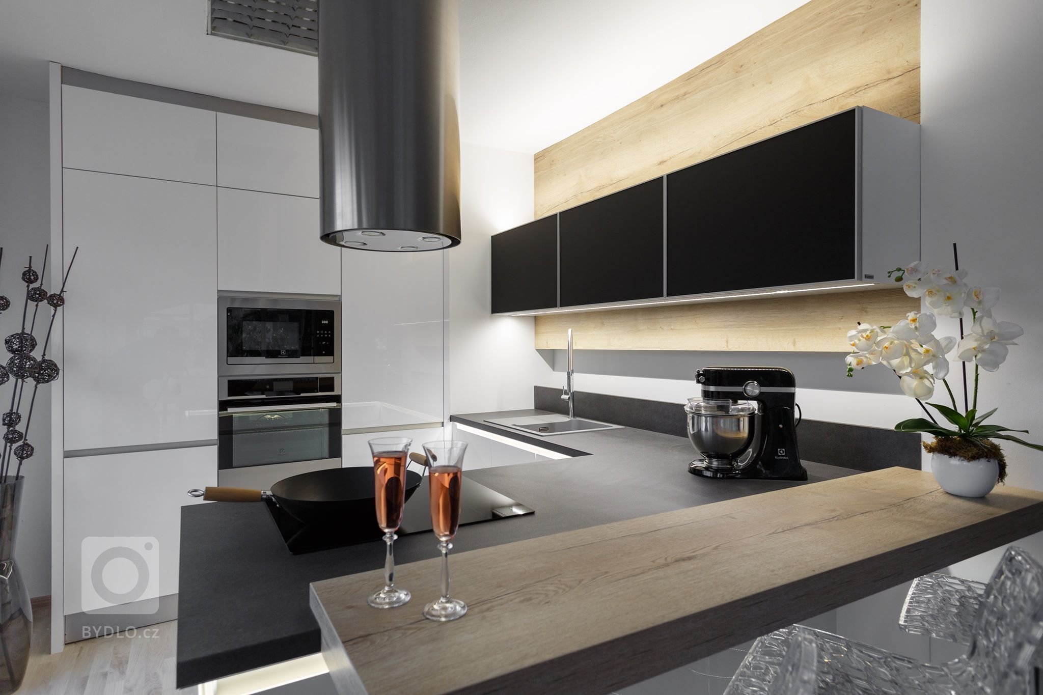 Chytré Kuchyně - bílý lesk s výraznou černou pracovní deskou a nadčasovým dřevodekorem s neparavidelnou kresbou.&nbsp;
