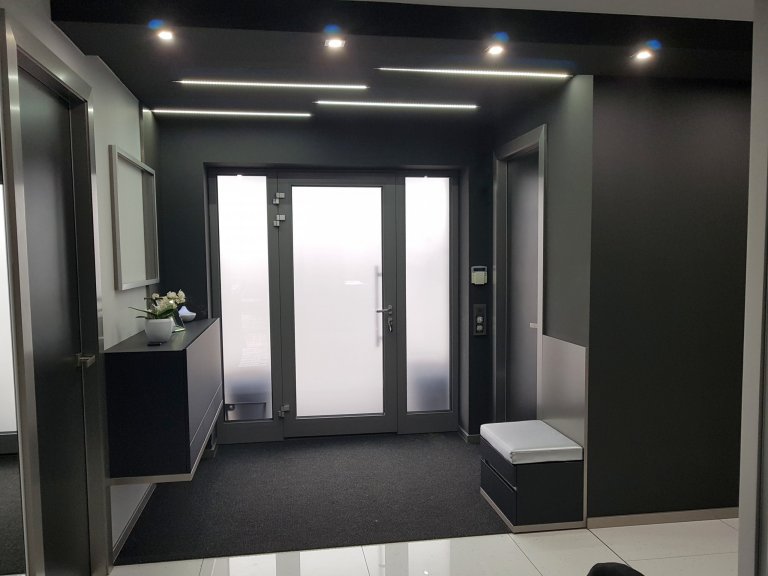 Snížený strop ve vstupu přechází da další snížené části v dlouhé chodbě s bodovkami z černého skla. 