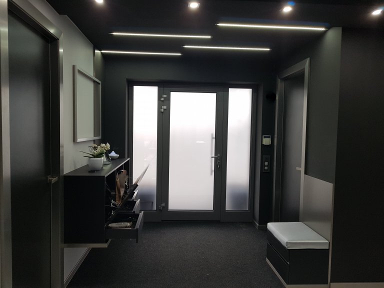 Strop je snížený v černém provedení se zapuštěnými LED pásky. 