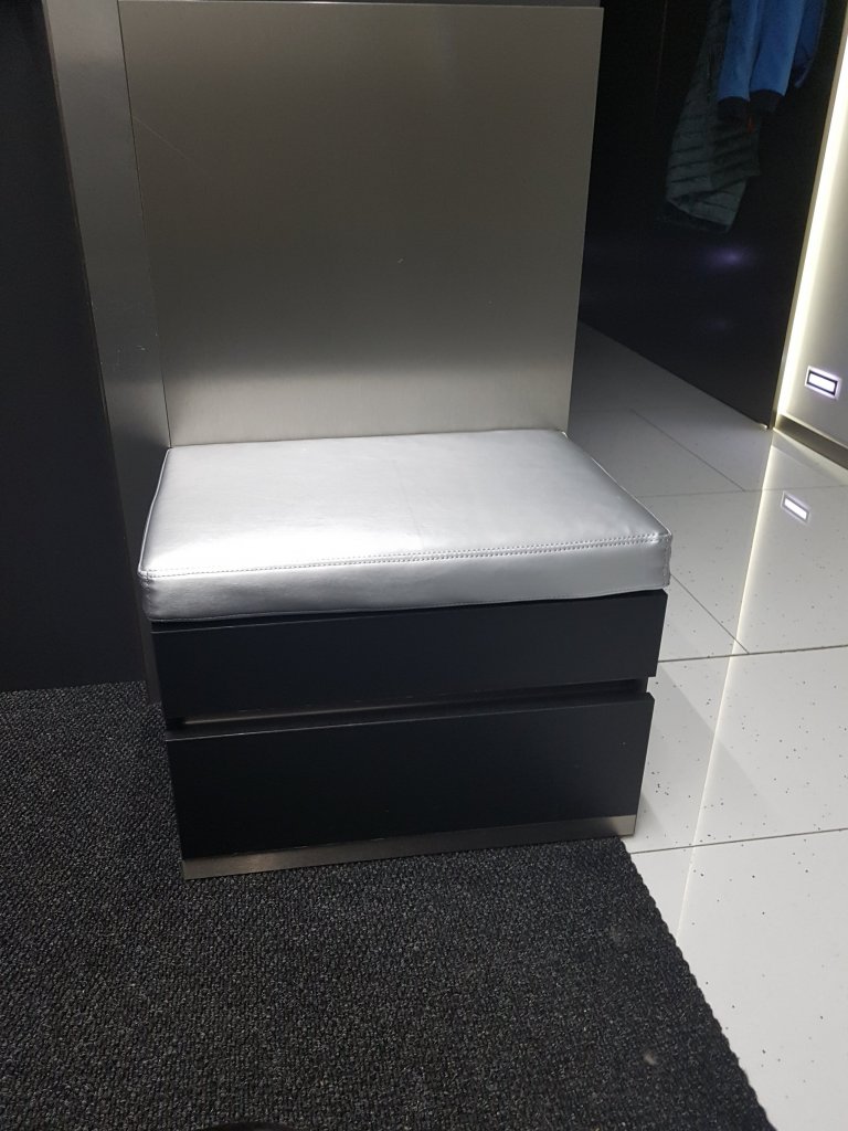 Proti komodě je taburetka na sednutí a zutí bot.  