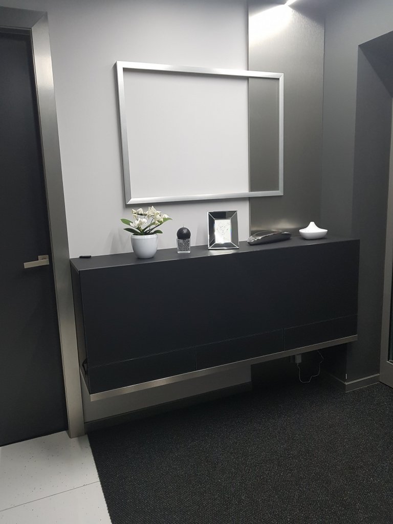 Prostor za vstupními dveřmi je sice prostorný, ale hodně rozbitý. Vždy zbývá pouze kousek stěny. Přímo u dveří je komoda se sklopnými dveřmi na kabelky a zásuvkami na drobnosti jako jsou brýle aj. Na zdi je připravený stříbrný obrazový rám na rodinnou fotografii.