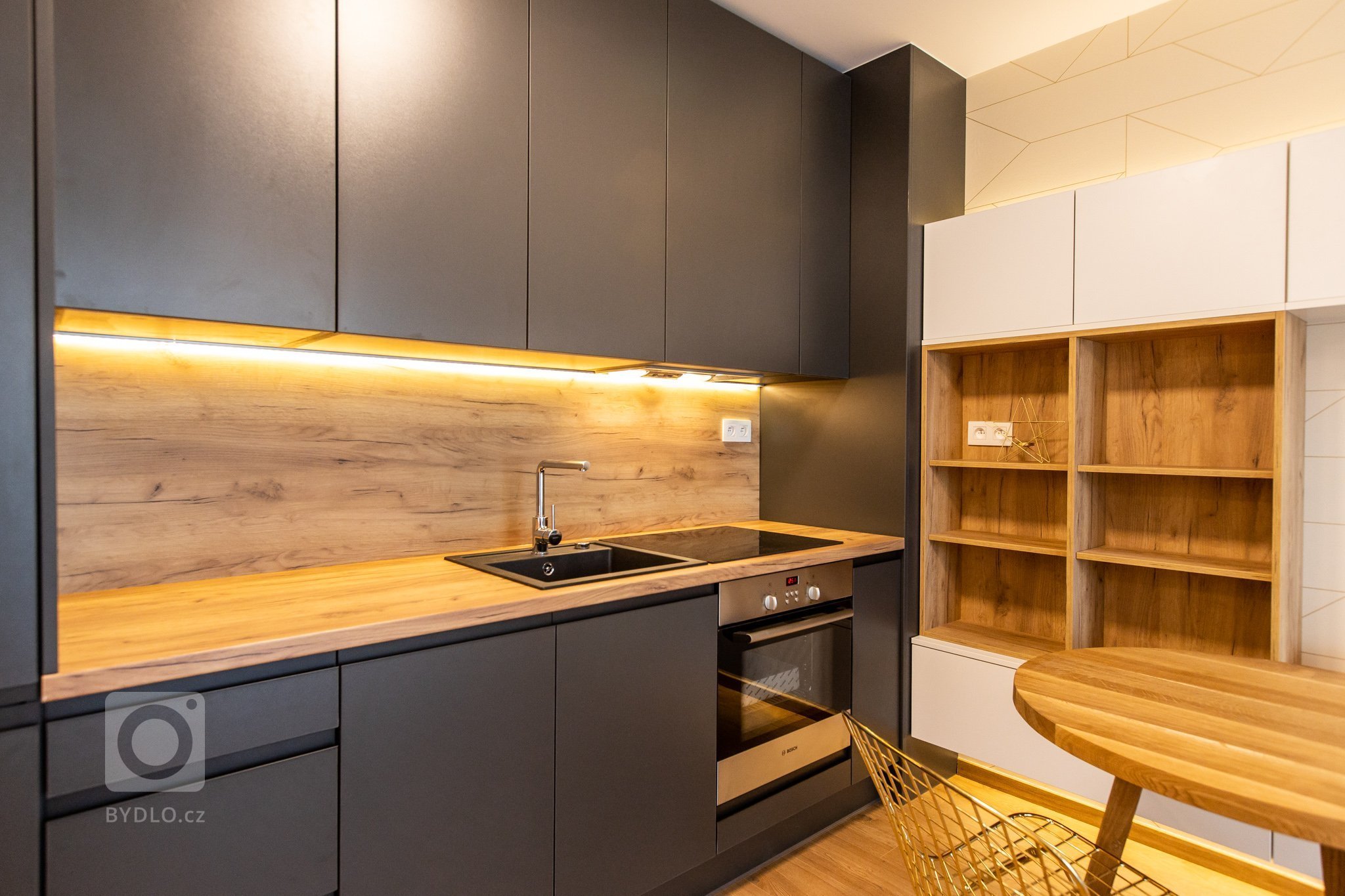 Krásna realizácia, ktorá dokonale prepája antracitovú kuchyňu s bielou obývacou zostavou.
