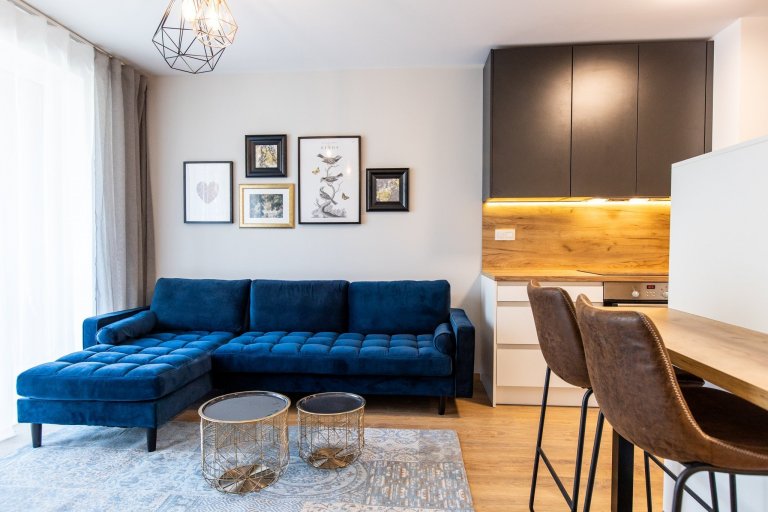 Krásne minimalisticky zariadený byt v Urban Residence, ktorého dominantou je modrá rohová sedačka. Kuchynská linka je krásne ladená v tónoch ceého bytu, aby…