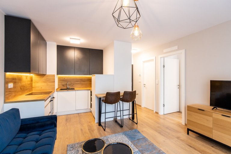 Krásne minimalisticky zariadený byt v Urban Residence, ktorého dominantou je modrá rohová sedačka. Kuchynská linka je krásne ladená v tónoch ceého bytu, aby…