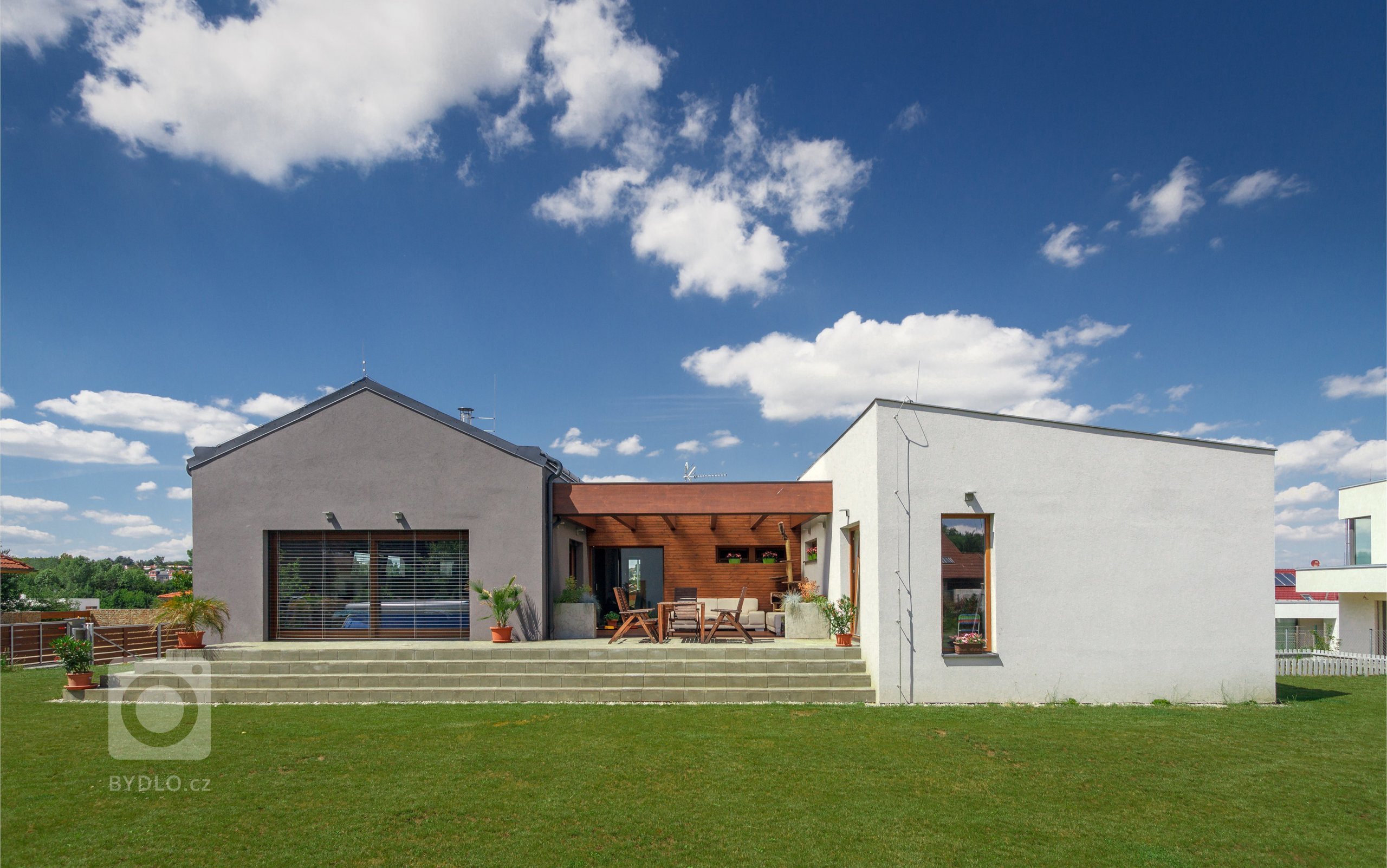 Dům je umístěn v severní části pozemku a otevírá se velkým francouzským oknem a atriem na jih do zahrady. Svou formou - tvarem střech a velikostí hmot -…