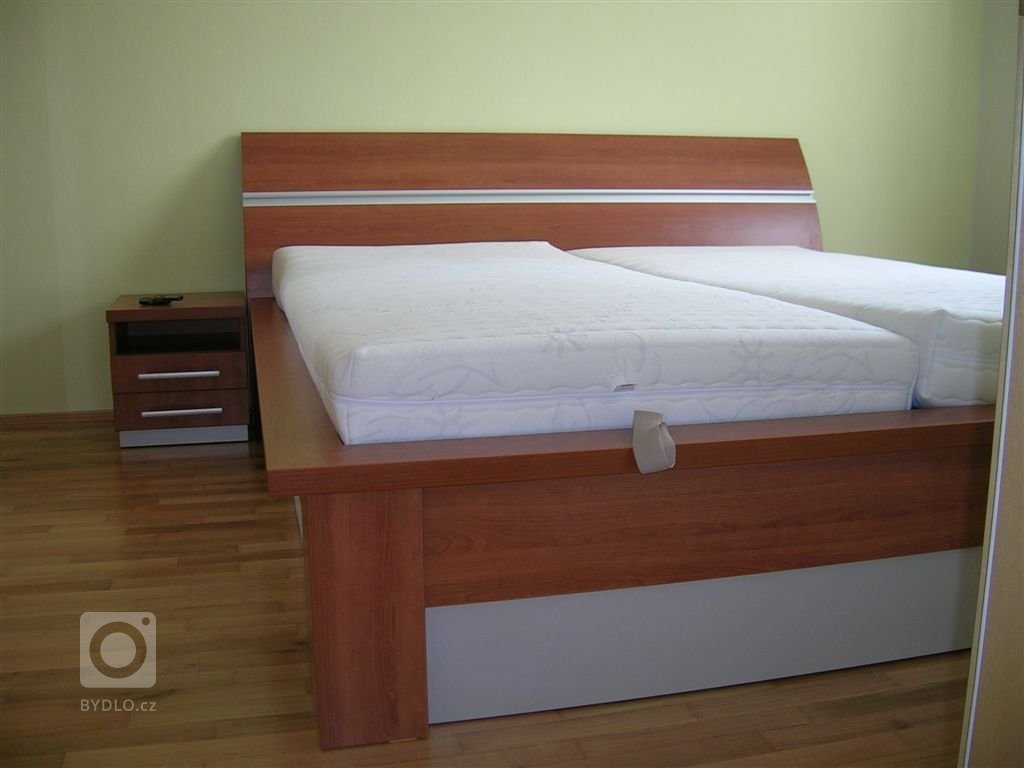 Ložnice s postelí s úložným prostorem, nočními stolky a vestavěnou skříní.
