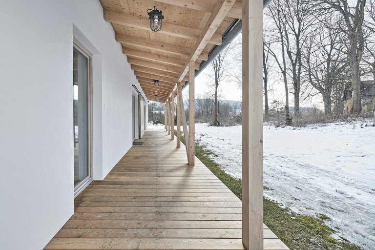 Pozemek leží na hraně svahu v&nbsp;centru malé obce na Vysočině. Na půdorysné stopě bývalého statku vznikl dům a stodola. Dům má podél jihozápadní fasády kryté…