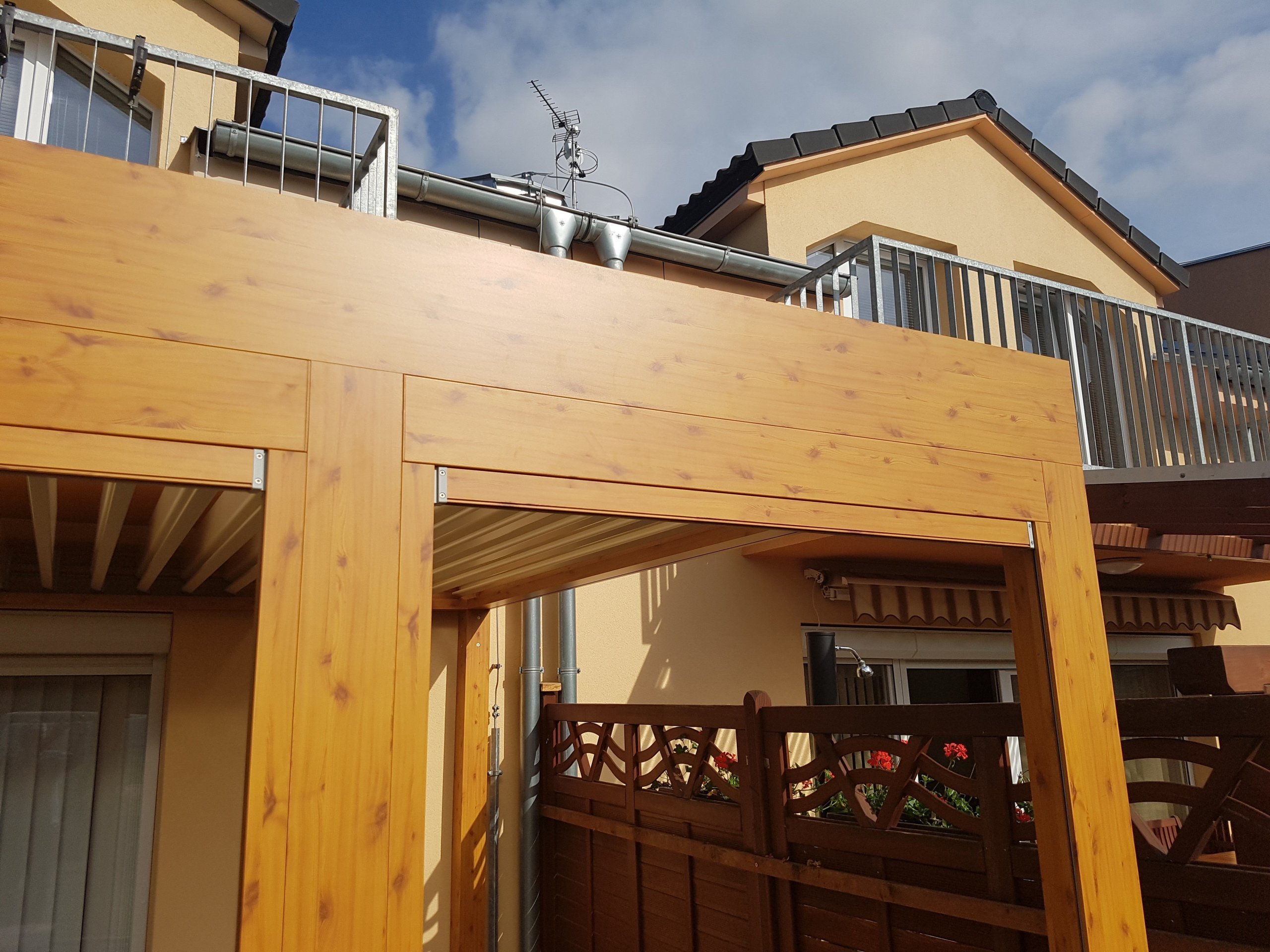 Lamelová pergola v imitaci dřeva a screenové rolety v husté zástavbě.
