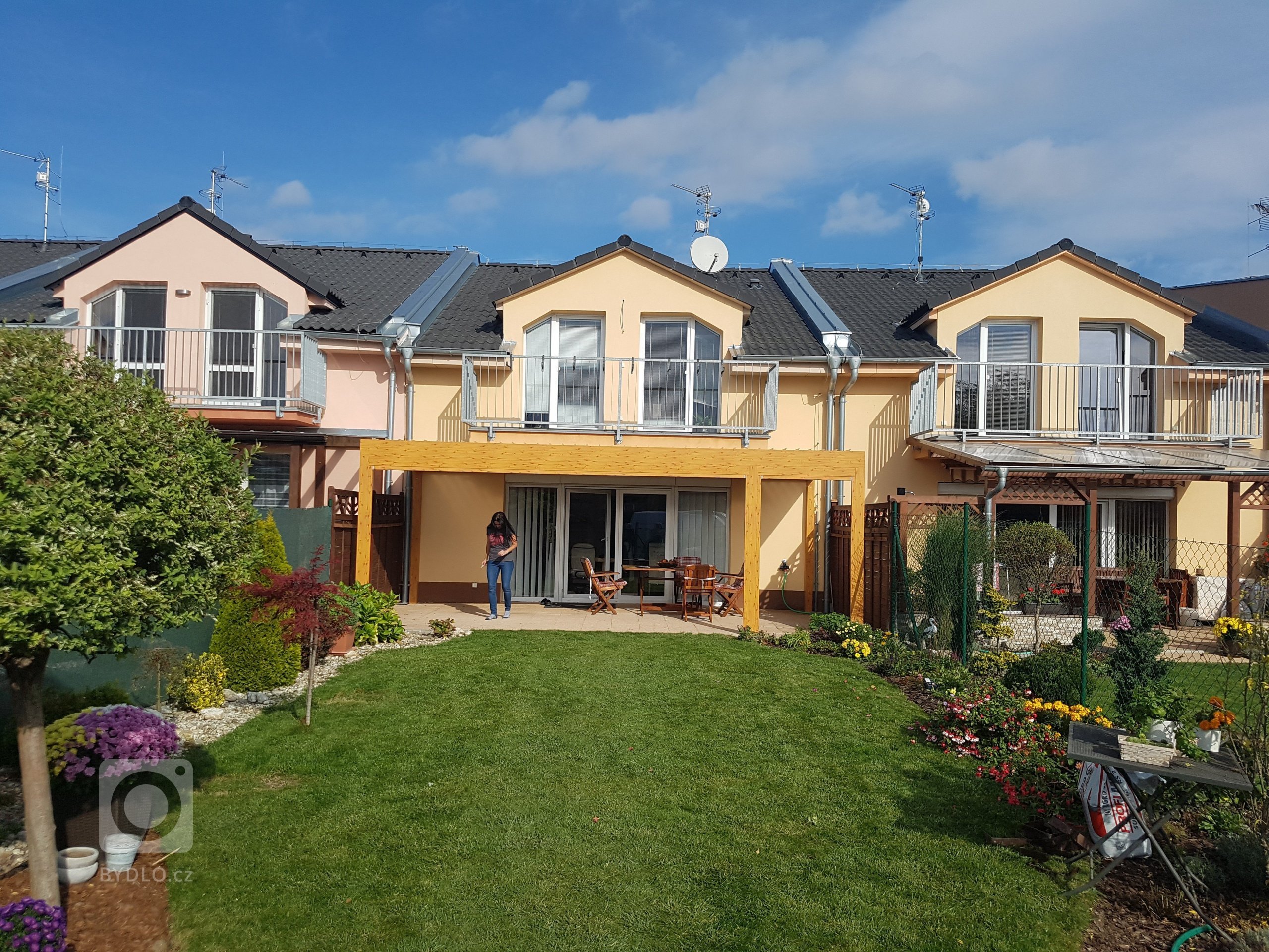 Lamelová pergola v imitaci dřeva a screenové rolety v husté zástavbě.
