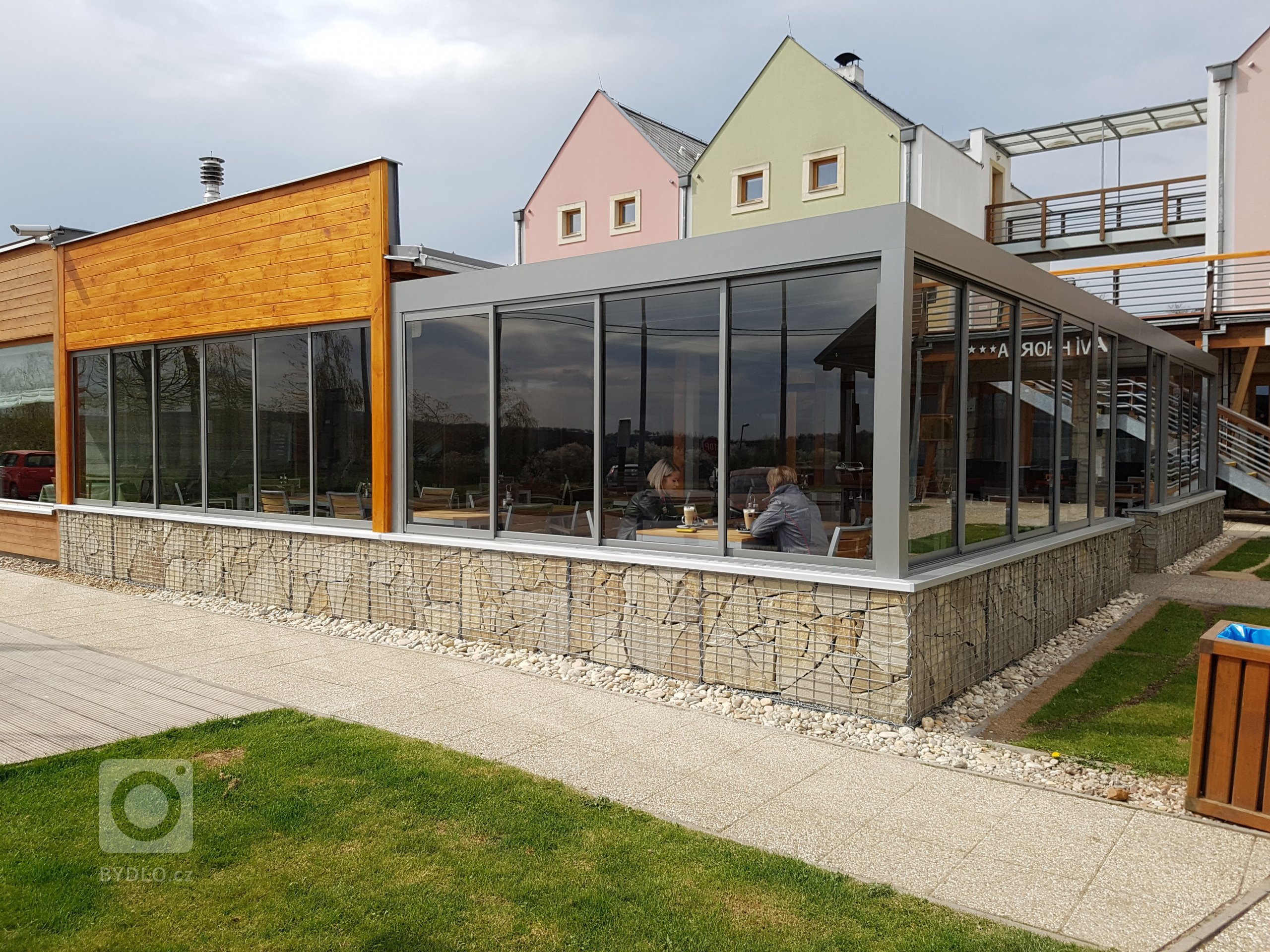 Hliníkovú pergolu jsme osvětlili a zavedli do ní všechny inženýrské sítě, díky čemuž se stala plnohodnotnou venkovní restaurací a barem.&nbsp;Boční zakrytí…
