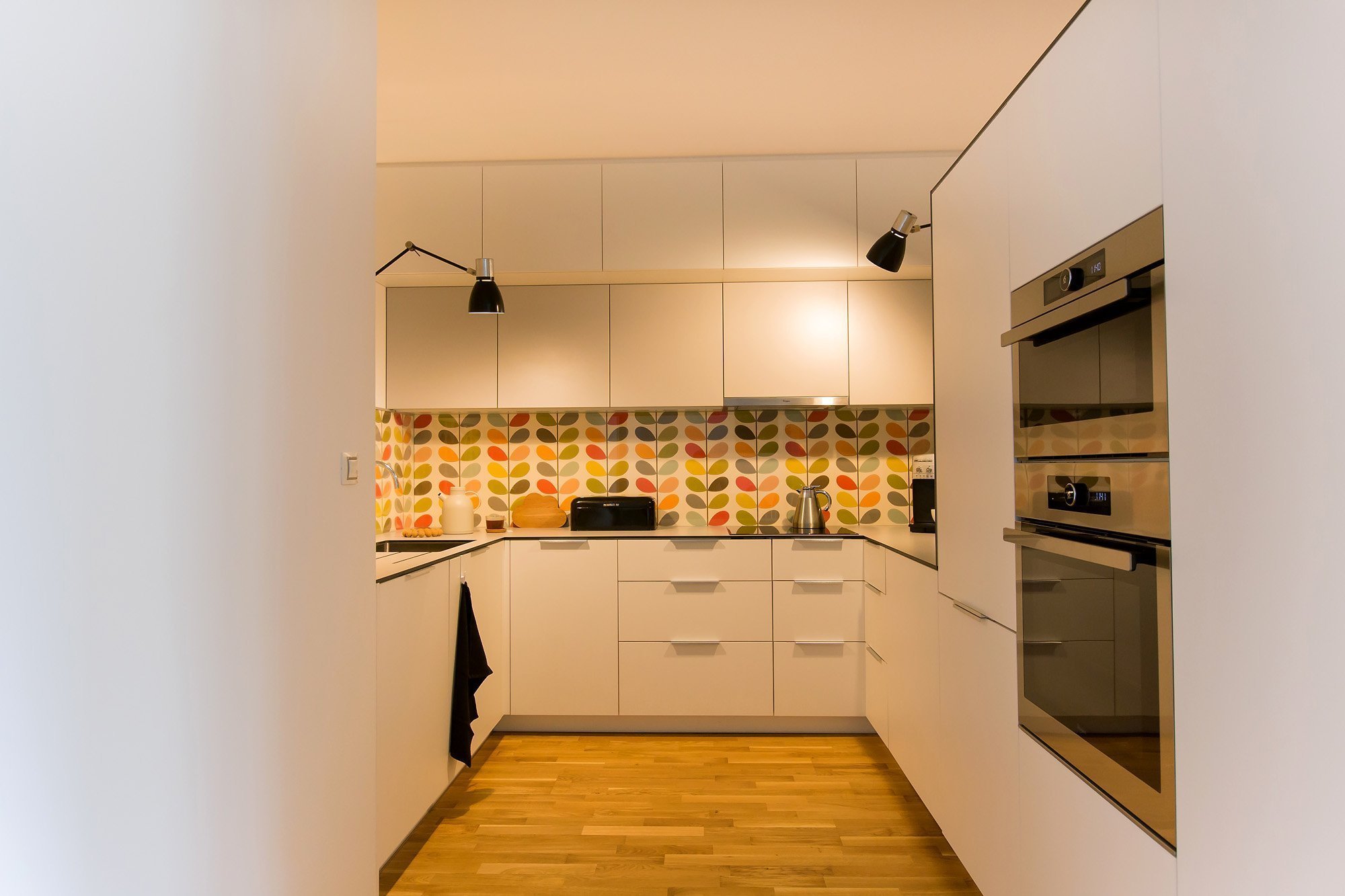 Koncept byl jasný- jednoduchá světlá linka vyladěná tapetou od Orly Kiely, která celý prostor rozzáří. Kuchyň se nachází v&nbsp;tmavém koutě bez okna, proto je…