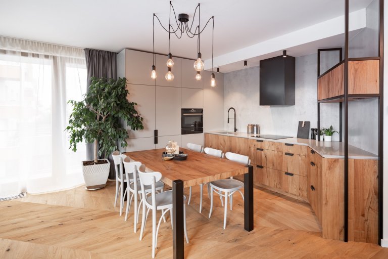 Netradiční tvar kuchyně byl vyřešen vysokou sestavou kuchyňských skříněk lakovaných světle šedou barvou, které volně navazují na pracovní desku z umělého kamene.