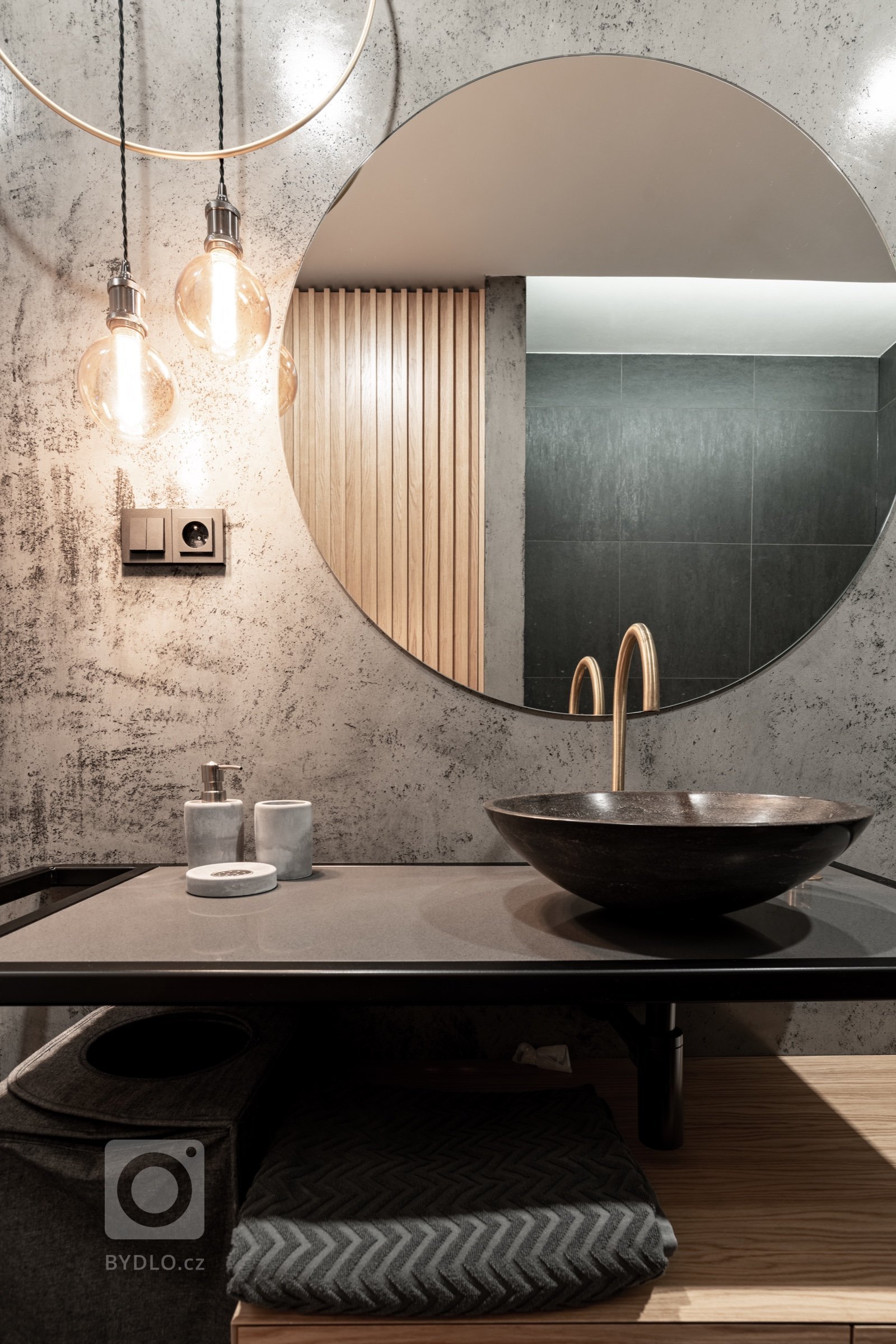 V koupelně u ložnice se jedná o zrcadlo podsvícené, v hlavní koupelně je doplněno o designový autorský prvek mosazné obruče, kombinované se závěsnými Edison žárovkami. 
