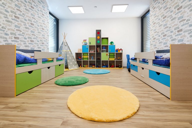 Když pro kluky tak zelená a modrá. Veselé skříňky na zakázku jsou dominantou pokoje a jejich originální provedení díky svítícímu semaforu se stává prostorem nejen pro hru, ale s úchytkami ve tvaru číslic i učení se k pořádku a počítání. Nejen kluci, ale i táta jsou milovníci aut a to se musí promítnout i v jejich pokoji. Vliesová tapeta v jednoduchém a stylovém designu s autíčky je umocněna i originálními veselými poličkami, jak jinak než ve tvaru auta. Protože si kluci hrají stále na zemi doporučila jsem jako doplněk kulaté barevné koberečky s protiskluzovou vrstvou.