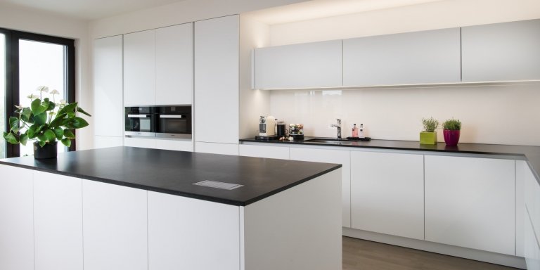 Kuchyň EGGERSMANN, byt, realizace 2018. Provedení je melamin Tarent 2700 KU bílá mat, bezúchytkový systém e:sing hliník, doplňky Blanco. Pracovní deska je žula…
