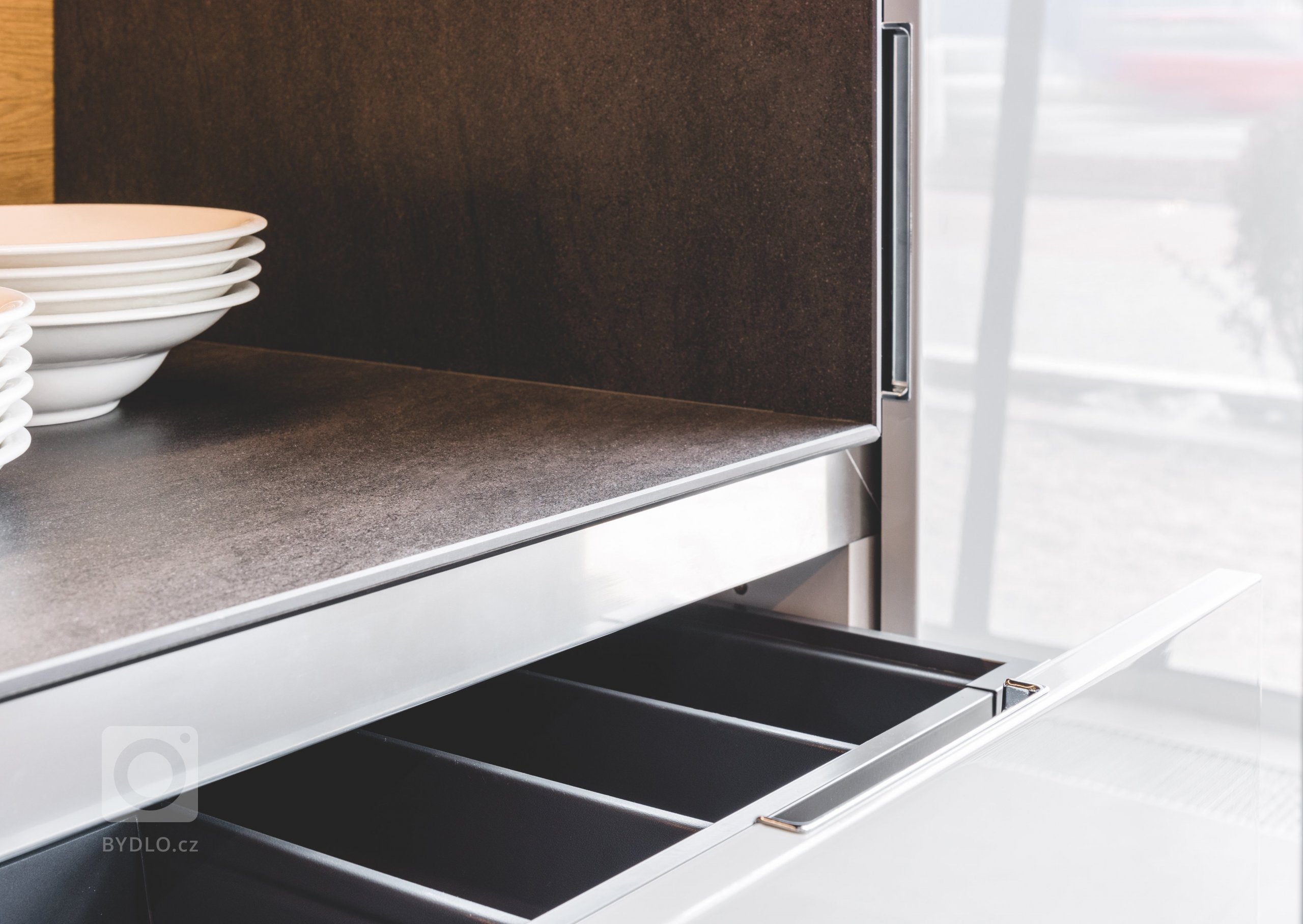 Vysoké skříně mají lakovaná dvířka v leštěném lesku ve dvou odstínech šedi, takže vám nikdy nezevšední. Napravo je do nich včleněna spotřebičová zóna,…