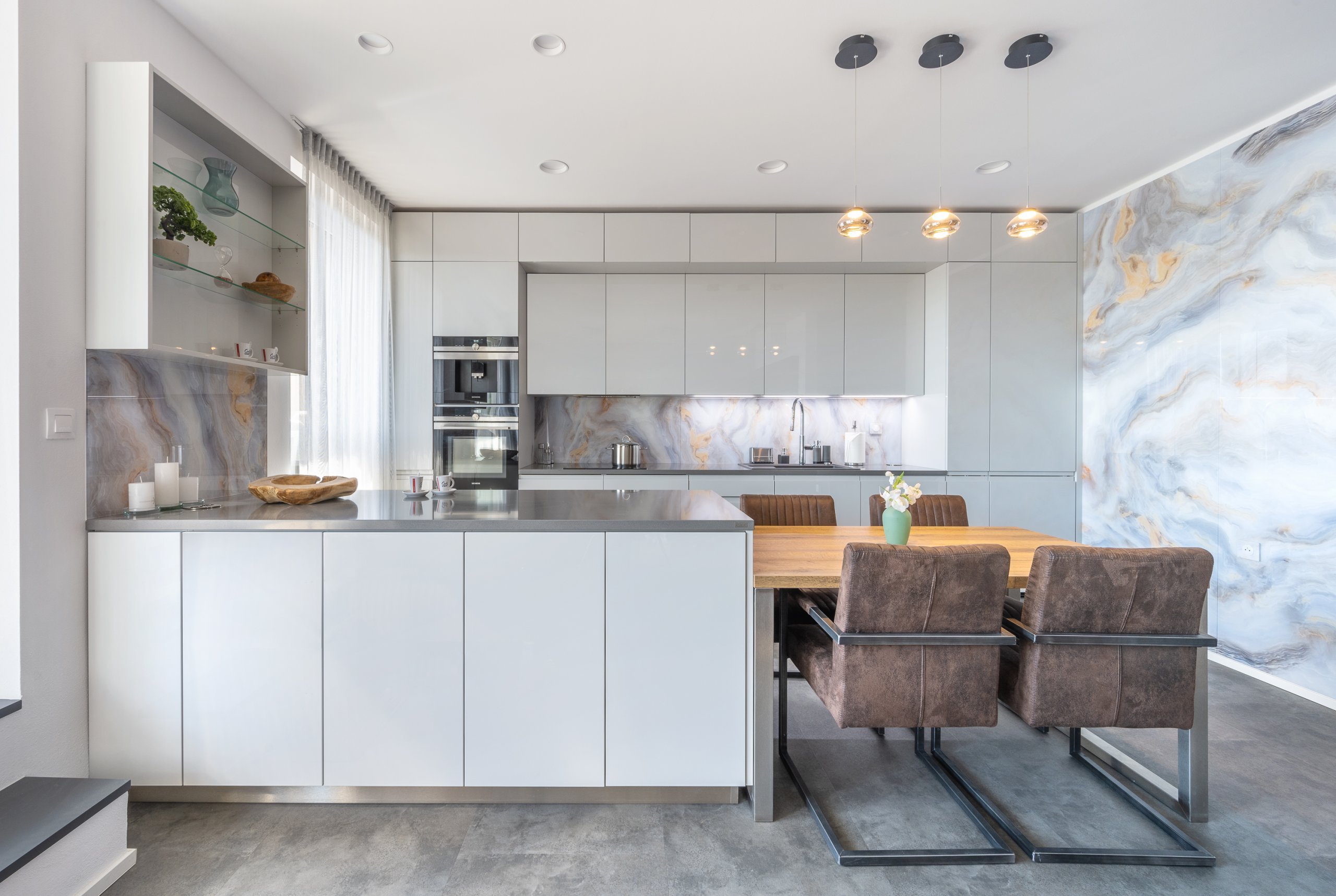 Sestava samotná využívá symetrii horních a dolních skříněk v provedení Light Grey. Bílé, leskle lakované plochy dvířek jsou okouzlující na pohled i vhodné na každodenní provoz. Ve spojení se zástěnami působí vzdušně a přidávají prostoru na velikosti. Zafrézované úchytky Pure už tak nepřehlédnutelnou hladkost a čistotu linií ještě vyzdvihují. Sestava samotná využívá symetrii horních a dolních skříněk v provedení Light Grey. Bílé, leskle lakované plochy dvířek jsou okouzlující na pohled i vhodné na každodenní provoz. Ve spojení se zástěnami působí vzdušně a přidávají prostoru na velikosti. Zafrézované úchytky Pure už tak nepřehlédnutelnou hladkost a čistotu linií ještě vyzdvihují.