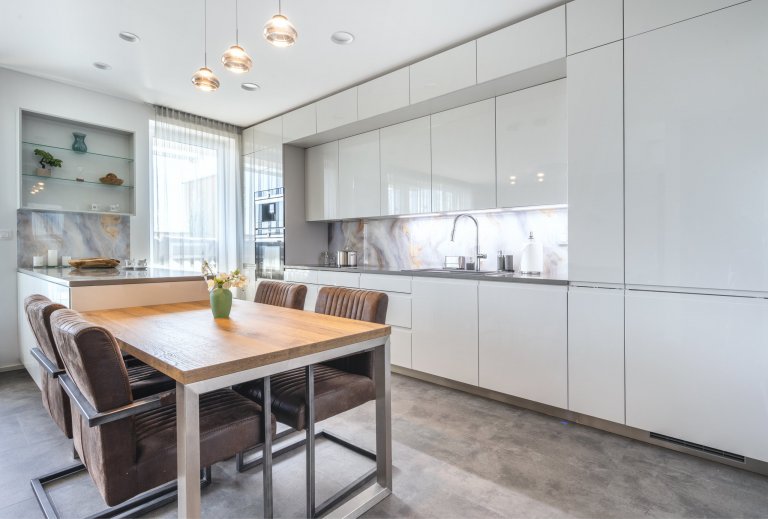 Sestava samotná využívá symetrii horních a dolních skříněk v provedení Light Grey. Bílé, leskle lakované plochy dvířek jsou okouzlující na pohled i vhodné na každodenní provoz. Ve spojení se zástěnami působí vzdušně a přidávají prostoru na velikosti. Zafrézované úchytky Pure už tak nepřehlédnutelnou hladkost a čistotu linií ještě vyzdvihují.