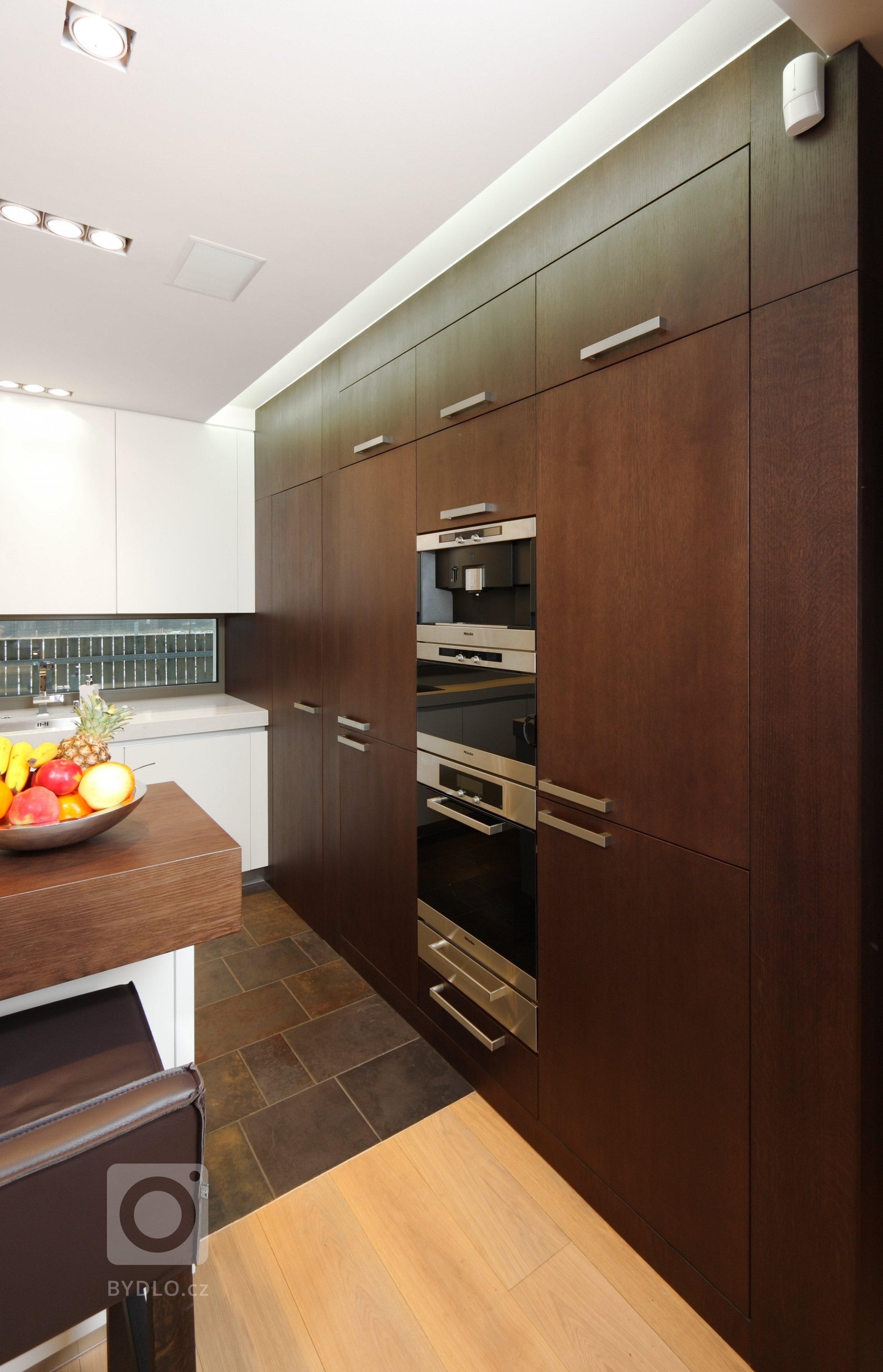 Prostorná a impozantní kuchyň s ostrůvkem, plná odvážných hran a kontrastů. Lakované povrchy střídají tmavou barvu s bílou a podtrhují tak její minimalistický…