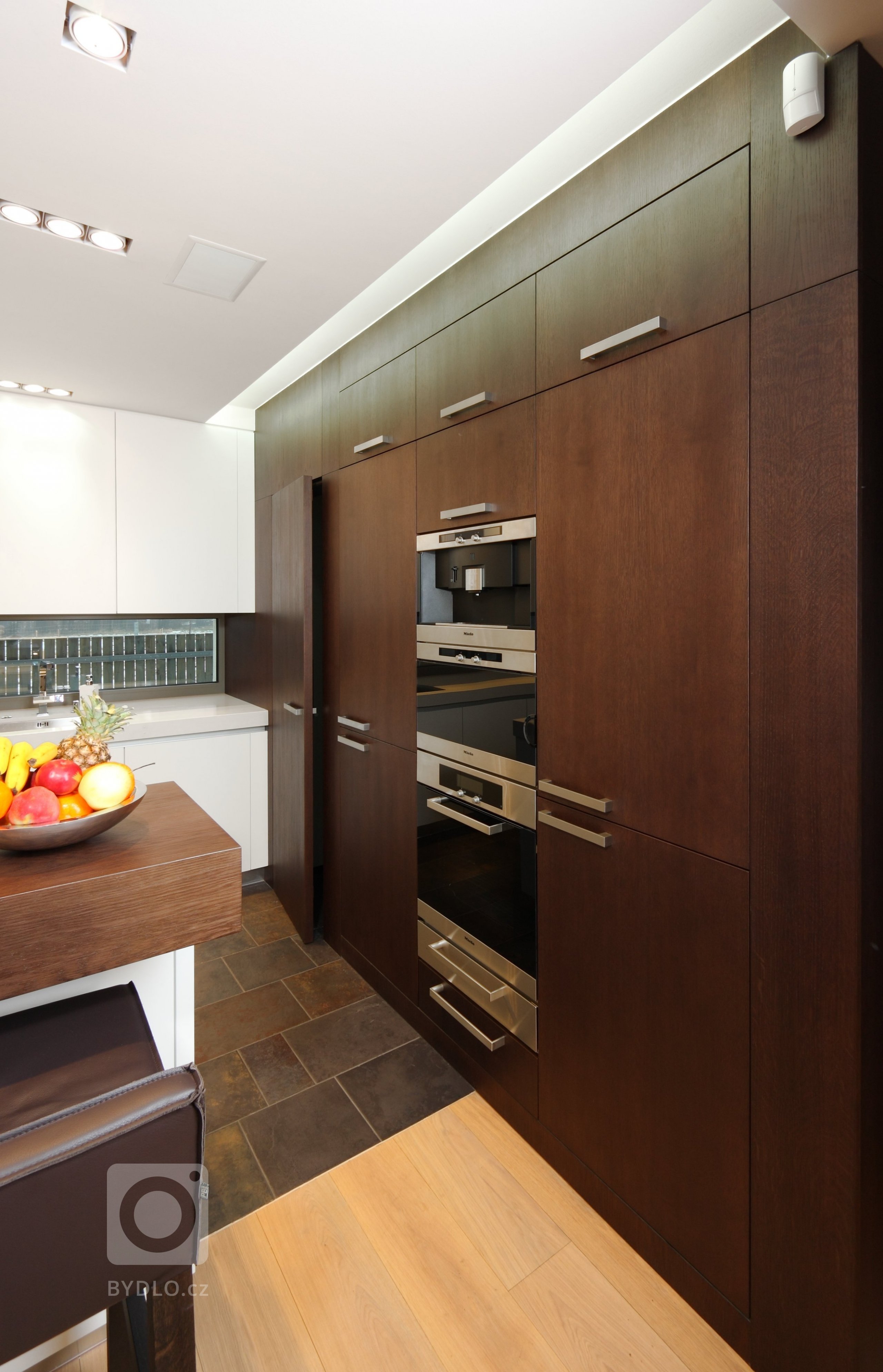 Prostorná a impozantní kuchyň s ostrůvkem, plná odvážných hran a kontrastů. Lakované povrchy střídají tmavou barvu s bílou a podtrhují tak její minimalistický…