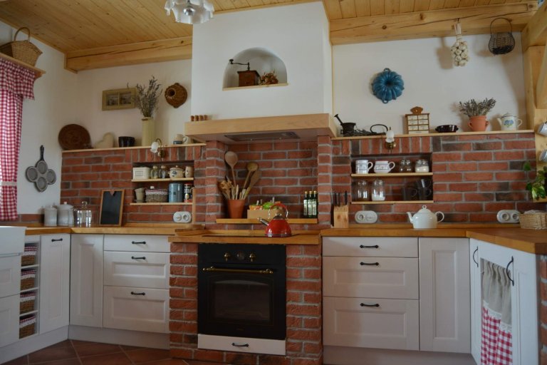 Prostorná rustikální kuchyně s&nbsp;moderními spotřebiči, doplněna památečnými kousky (formy, mlýnky, ošatky atd.) a cihlovým obkladem pro navození požadované…