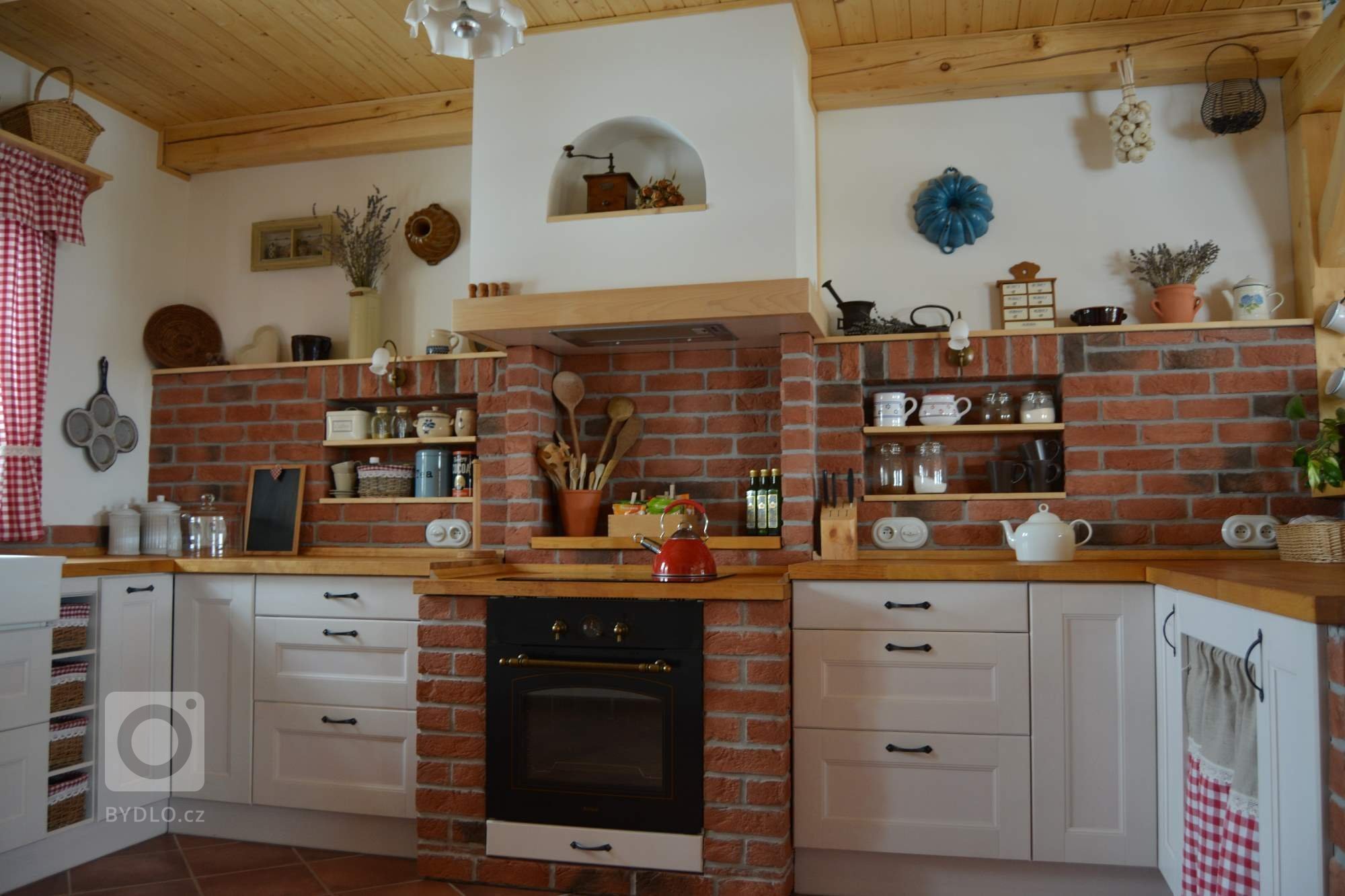Prostorná rustikální kuchyně s&nbsp;moderními spotřebiči, doplněna památečnými kousky (formy, mlýnky, ošatky atd.) a cihlovým obkladem pro navození požadované…