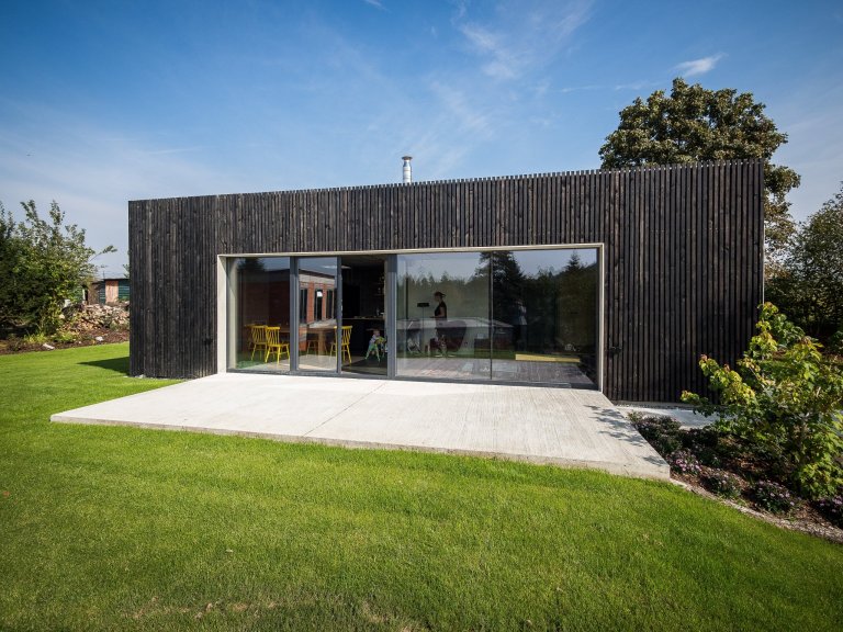 Jednoduchou hmotu ZEN HOME zdobí fasáda z hrubého černého dřeva a velké prosklení.